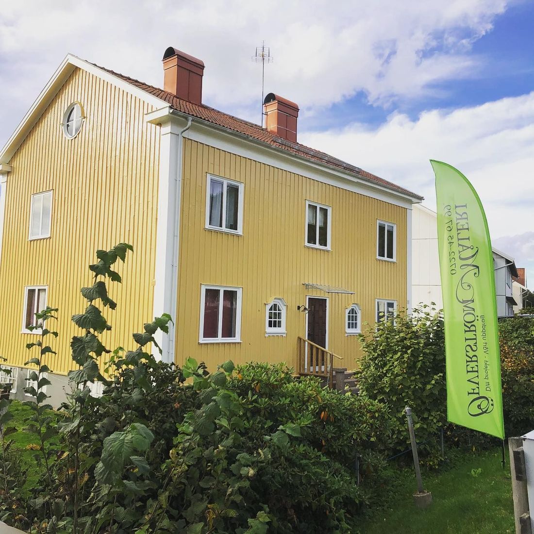 Öfverström Måleris gröna beachflagga uppställd framför ett gult trähus under pågående arbete.